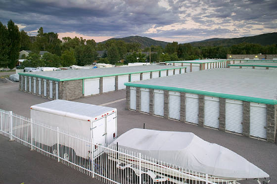 Outdoor storage at All Hours Storage with a tarp covered boat on a trailer and an enclosed utility trailer parked inside the fenced lot
